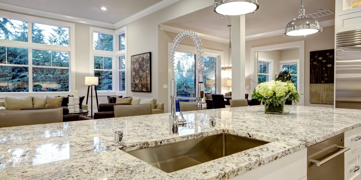 White kitchen design features large bar style kitchen island with granite countertop illuminated by modern pendant lights. Northwest, USA
